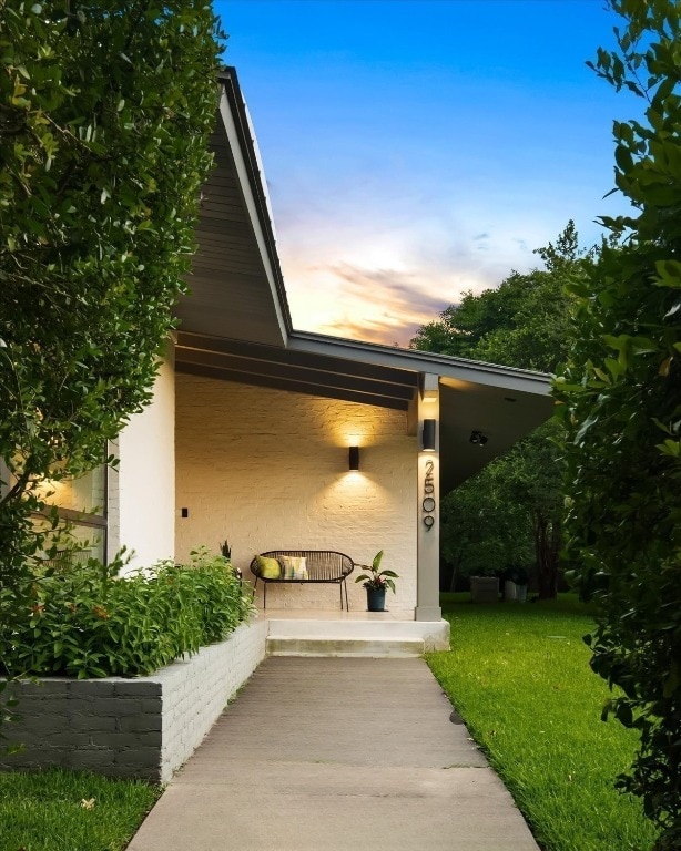 entrance to property with a porch, stucco siding, and a yard