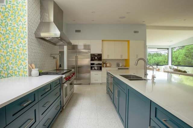 kitchen with wall chimney range hood, high quality appliances, visible vents, and a sink