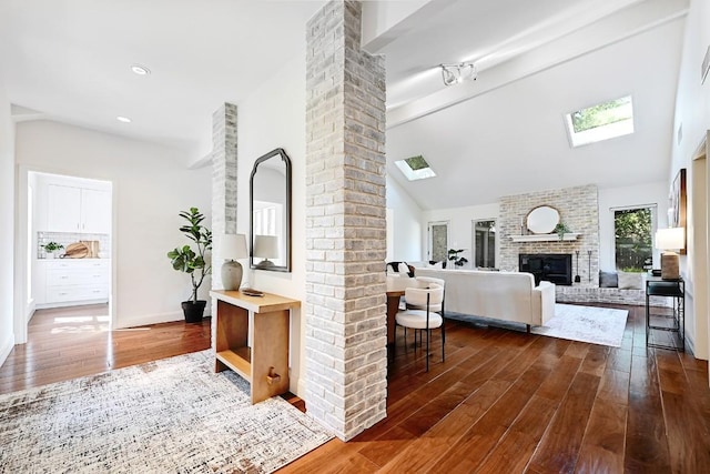 interior space with dark wood-style flooring, decorative columns, a fireplace, high vaulted ceiling, and a skylight