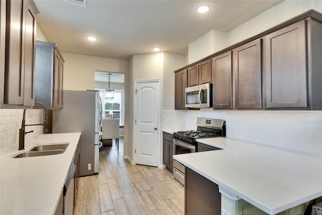 kitchen featuring decorative backsplash, appliances with stainless steel finishes, a sink, a peninsula, and light wood-style flooring
