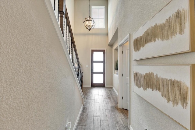doorway to outside with a towering ceiling, wood finished floors, stairway, baseboards, and a chandelier