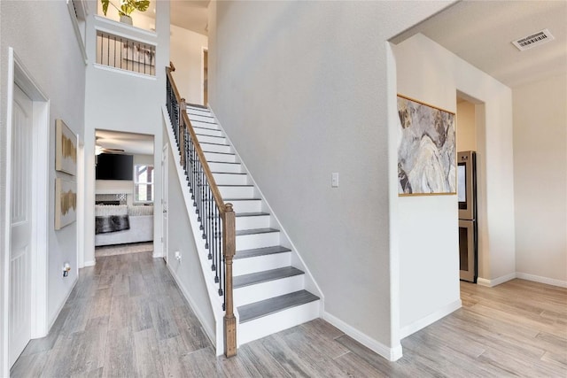staircase with a fireplace, a ceiling fan, baseboards, wood finished floors, and visible vents