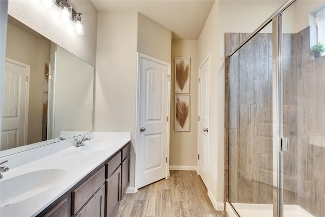 bathroom featuring double vanity, a sink, wood finished floors, and a shower stall