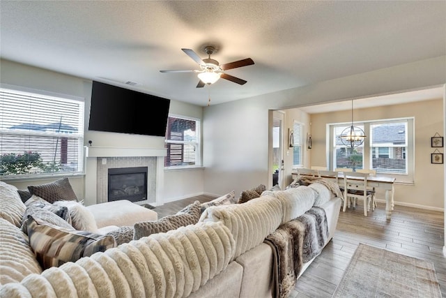 living room with visible vents, a glass covered fireplace, wood finished floors, baseboards, and ceiling fan with notable chandelier