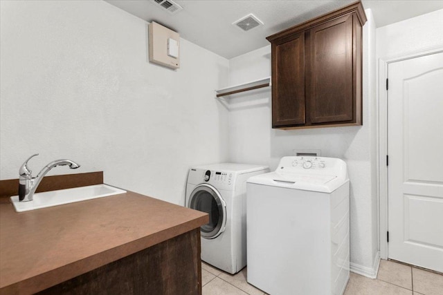 laundry area featuring visible vents, washing machine and dryer, cabinet space, a sink, and light tile patterned flooring
