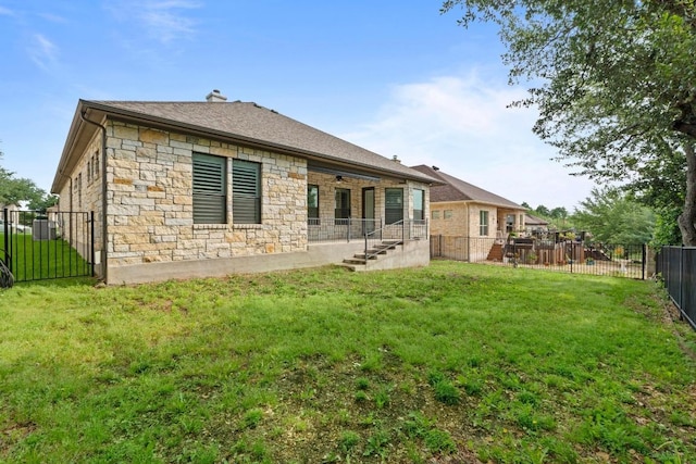 rear view of house featuring a lawn, ceiling fan, a fenced backyard, and stone siding