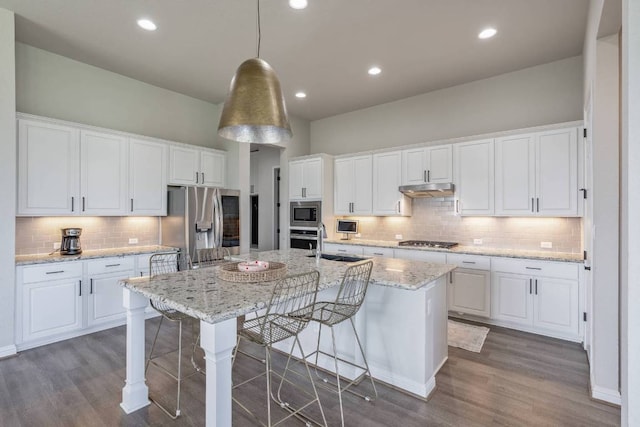 112 Bittik Cv, Georgetown, TX 78628 - kitchen featuring stainless steel appliances, decorative backsplash, under cabinet range hood, an island with sink, and white cabinets