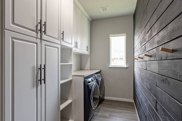 112 Bittik Cv, Georgetown, TX 78628 - laundry area with cabinet space, washing machine and dryer, light wood finished floors, and wood walls