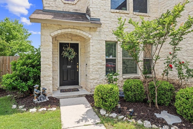 view of exterior entry featuring fence and stone siding