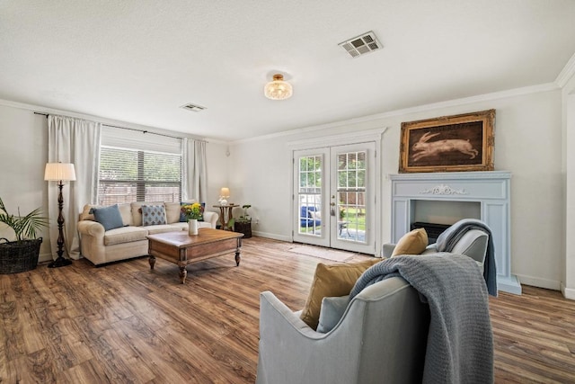 living room featuring visible vents, baseboards, crown molding, and wood finished floors