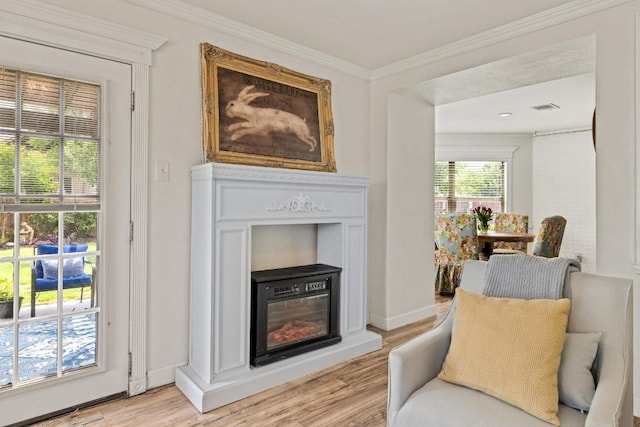 sitting room with a glass covered fireplace, ornamental molding, light wood-style flooring, and visible vents