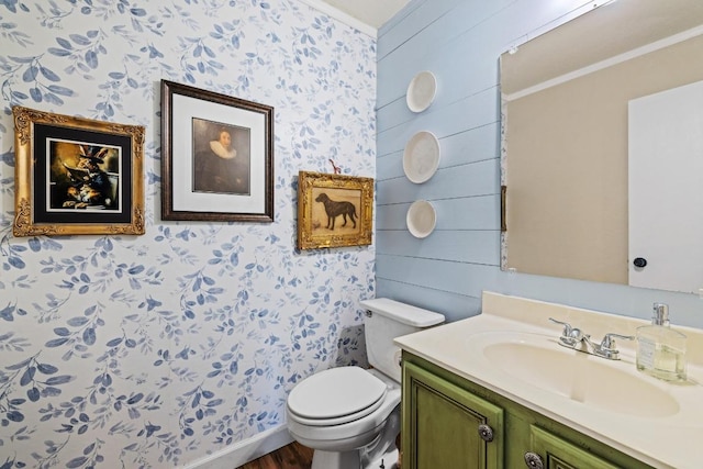 bathroom featuring wood finished floors, vanity, toilet, ornamental molding, and wallpapered walls
