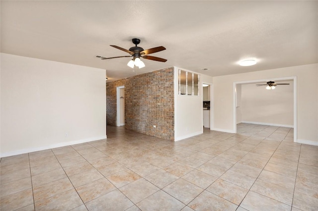 spare room featuring baseboards, ceiling fan, light tile patterned floors, and brick wall