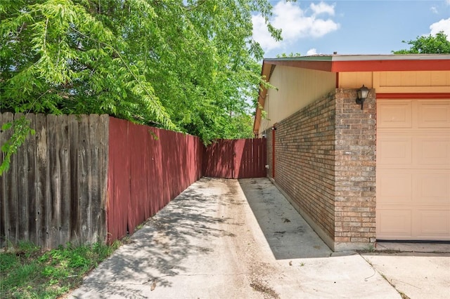 view of side of home with fence, a garage, and brick siding