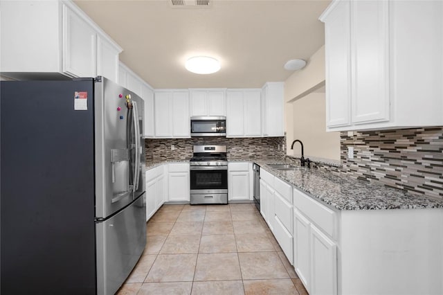 kitchen with decorative backsplash, appliances with stainless steel finishes, a sink, light tile patterned floors, and white cabinetry