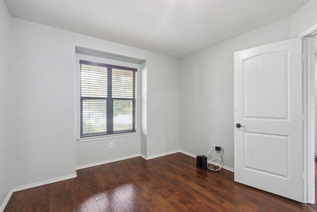 unfurnished room with baseboards and dark wood-style floors