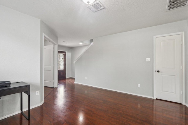 empty room with a textured ceiling, baseboards, visible vents, and wood finished floors
