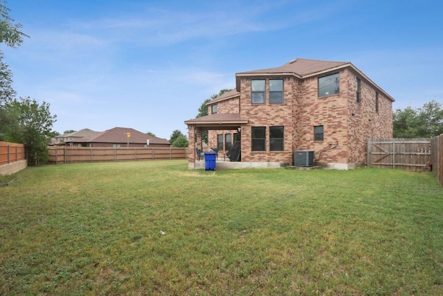 rear view of property featuring a lawn, brick siding, central AC unit, and a fenced backyard
