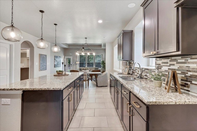 kitchen with hanging light fixtures, light stone counters, a sink, a center island, and decorative backsplash
