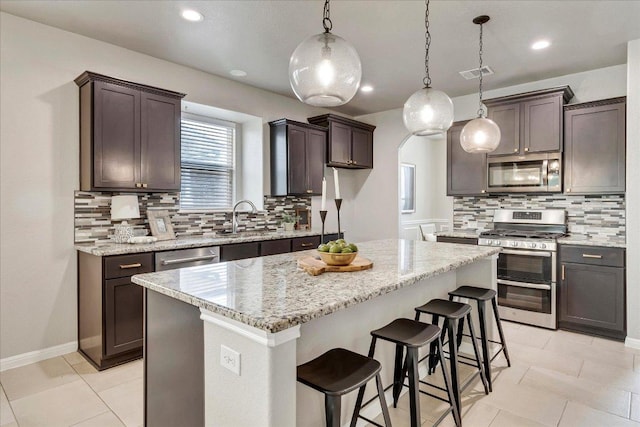 5684 Sabbia Dr, Round Rock, TX 78665 - kitchen featuring appliances with stainless steel finishes, decorative backsplash, light stone counters, dark brown cabinets, and a kitchen bar