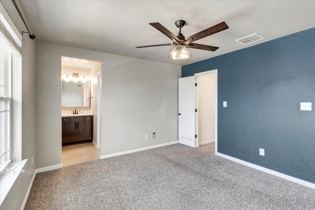 unfurnished bedroom featuring visible vents, a sink, baseboards, and light carpet