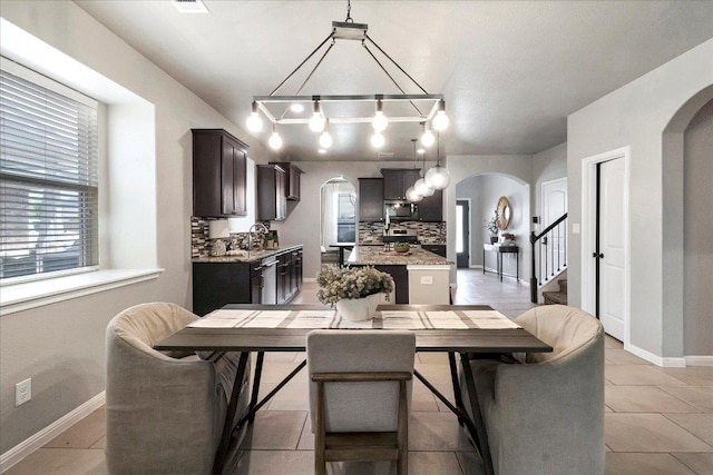 5684 Sabbia Dr, Round Rock, TX 78665 - dining room featuring arched walkways, a chandelier, stairs, and light tile patterned flooring