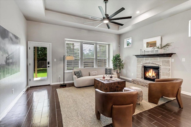 living area with wood tiled floor, a ceiling fan, a fireplace, baseboards, and a tray ceiling