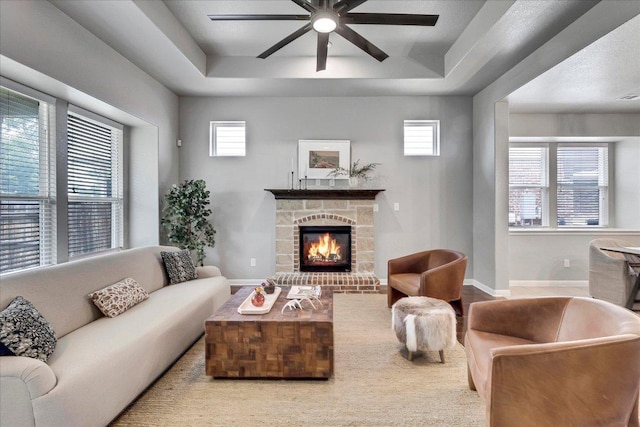 living area featuring a tray ceiling, plenty of natural light, ceiling fan, and a fireplace