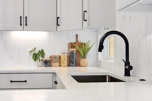 room details featuring a sink, decorative backsplash, white cabinetry, and light stone countertops
