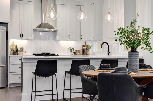1806 Maple Ave Unit 1, Austin, TX 78702 - kitchen featuring wall chimney exhaust hood, a kitchen breakfast bar, light countertops, decorative backsplash, and white cabinets