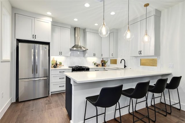 kitchen featuring light countertops, gas stove, a sink, freestanding refrigerator, and wall chimney exhaust hood