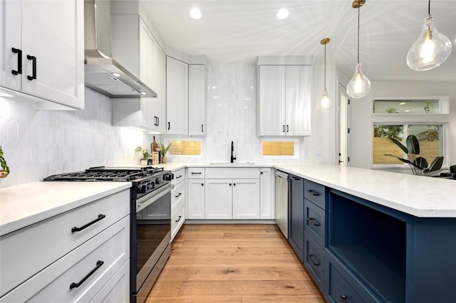 kitchen with wall chimney range hood, white cabinets, appliances with stainless steel finishes, a sink, and a peninsula