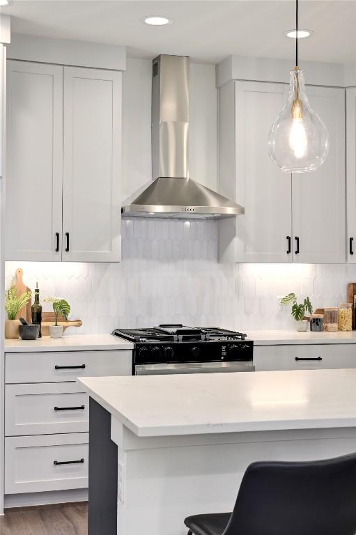 kitchen with wall chimney range hood, light countertops, stainless steel gas stove, and white cabinetry
