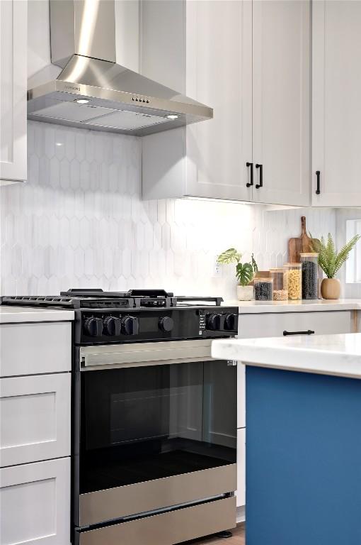 kitchen with stainless steel range with gas cooktop, wall chimney exhaust hood, backsplash, and white cabinetry