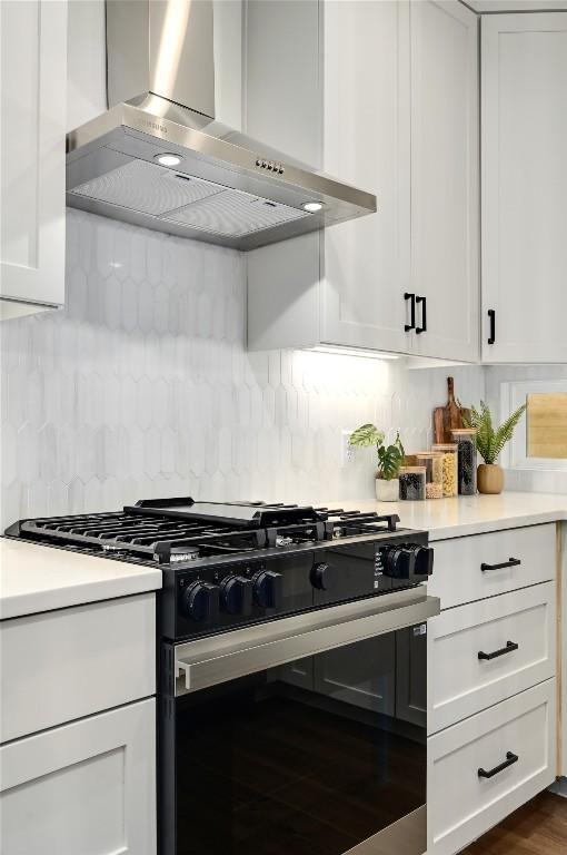 kitchen featuring light countertops, range with gas stovetop, wall chimney exhaust hood, and white cabinetry