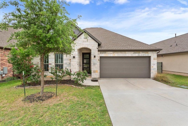 french provincial home with an attached garage, concrete driveway, a front yard, and stone siding