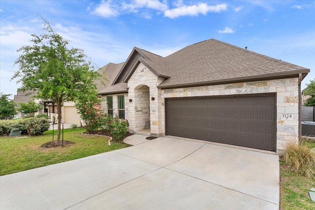 french country home featuring an attached garage, a front lawn, roof with shingles, and stone siding
