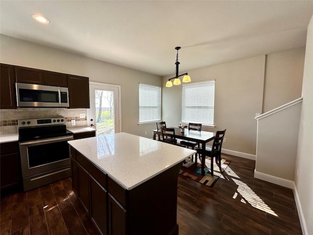 kitchen with dark wood finished floors, stainless steel appliances, decorative light fixtures, baseboards, and tasteful backsplash