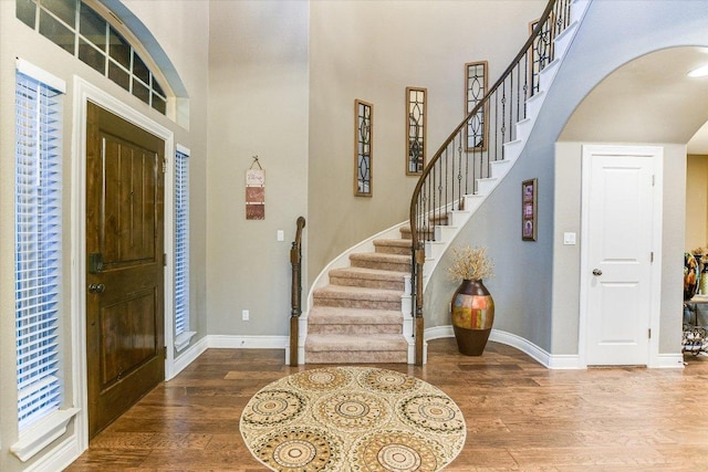 entrance foyer featuring baseboards, stairs, wood finished floors, and a high ceiling