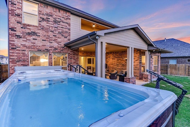 pool at dusk featuring fence and a hot tub