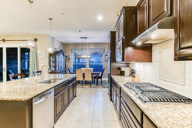 kitchen featuring appliances with stainless steel finishes, under cabinet range hood, a sink, backsplash, and dark brown cabinetry