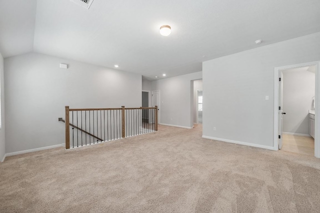 spare room with baseboards, vaulted ceiling, and light colored carpet