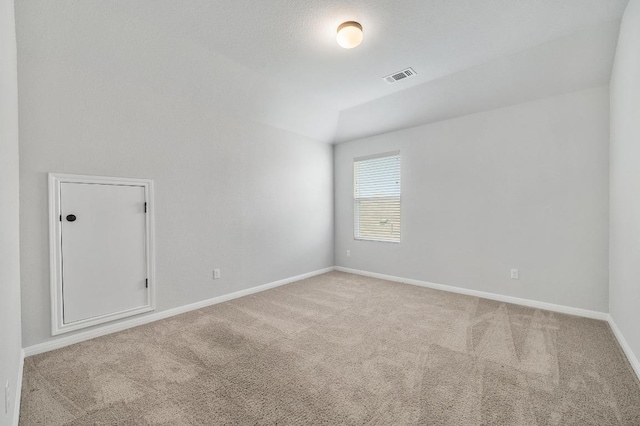 carpeted empty room featuring baseboards, visible vents, and vaulted ceiling
