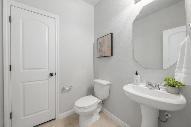 half bath with a sink, baseboards, tile patterned flooring, and toilet