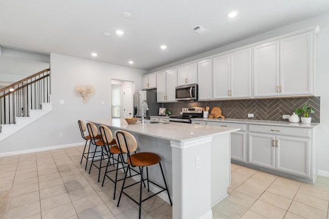 kitchen with appliances with stainless steel finishes, a breakfast bar, a sink, a kitchen island with sink, and decorative backsplash