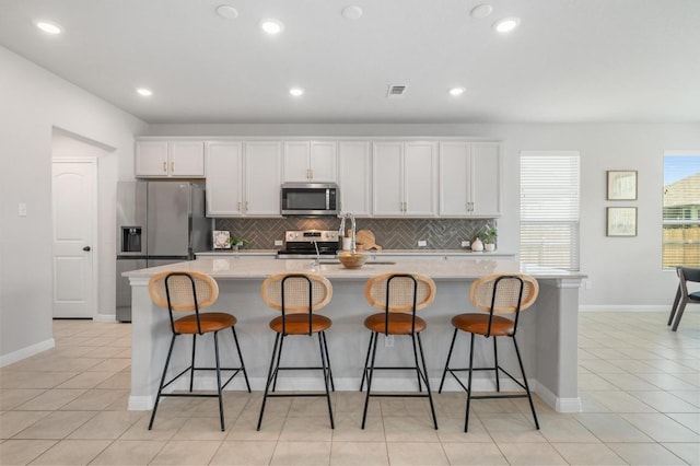 kitchen featuring appliances with stainless steel finishes, a sink, a kitchen island with sink, decorative backsplash, and visible vents