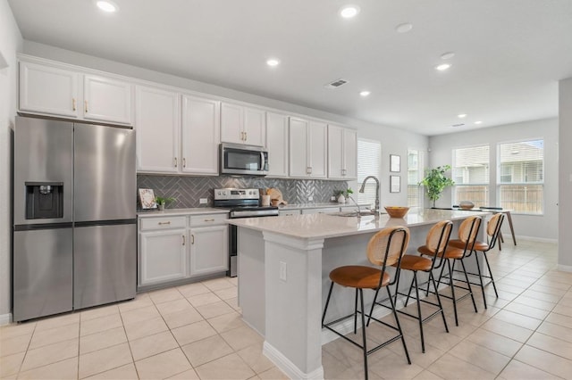 kitchen featuring backsplash, visible vents, a sink, stainless steel appliances, and an island with sink