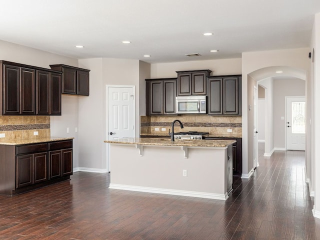 2040 Elaina Loop, Leander, TX 78641 - kitchen featuring stainless steel microwave, arched walkways, tasteful backsplash, light stone countertops, and dark wood-style floors