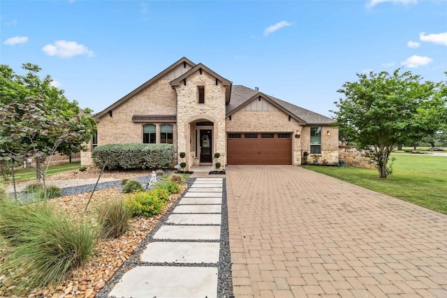 french country style house featuring stone siding, a front yard, decorative driveway, brick siding, and an attached garage