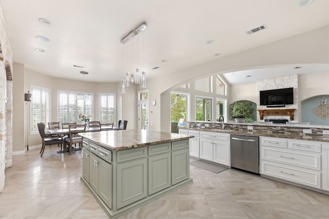 kitchen with light stone counters, a sink, a center island, stainless steel dishwasher, and visible vents